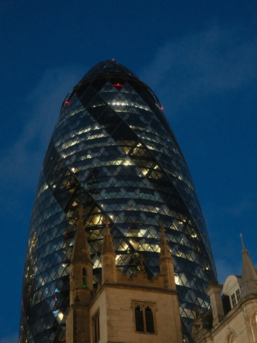 The Gherkin rising behind the tower of St Andrew Undershaft in the City of London at dusk
